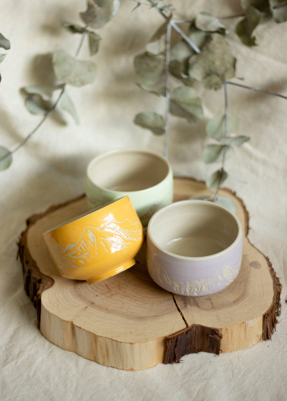 Image d'un trio de bols à thé aux couleurs Lilas, Mint et Orange doux. Ces bols utilisent la technique du sgraffito et sont gravés de paysages de Montagnes
