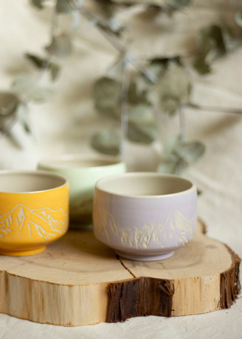 Image d'un trio de bols à thé aux couleurs Lilas, Mint et Orange doux. Ces bols utilisent la technique du sgraffito et sont gravés de paysages de Montagnes