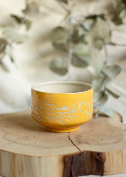 Image d'un bol à thé orange. Le bol est décoré en utilisant la technique du sgraffito et est gravé de paysages de Montagnes. 