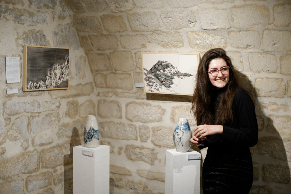 Photo de l'exposition The Spot dans laquelle on voit la potière Llaudem et ses créations: Deux tableaux de montagnes faits en carreaux de faïence émaillés et deux vases modelés décorés respectivement d'une montagne et d'une statue de femme.