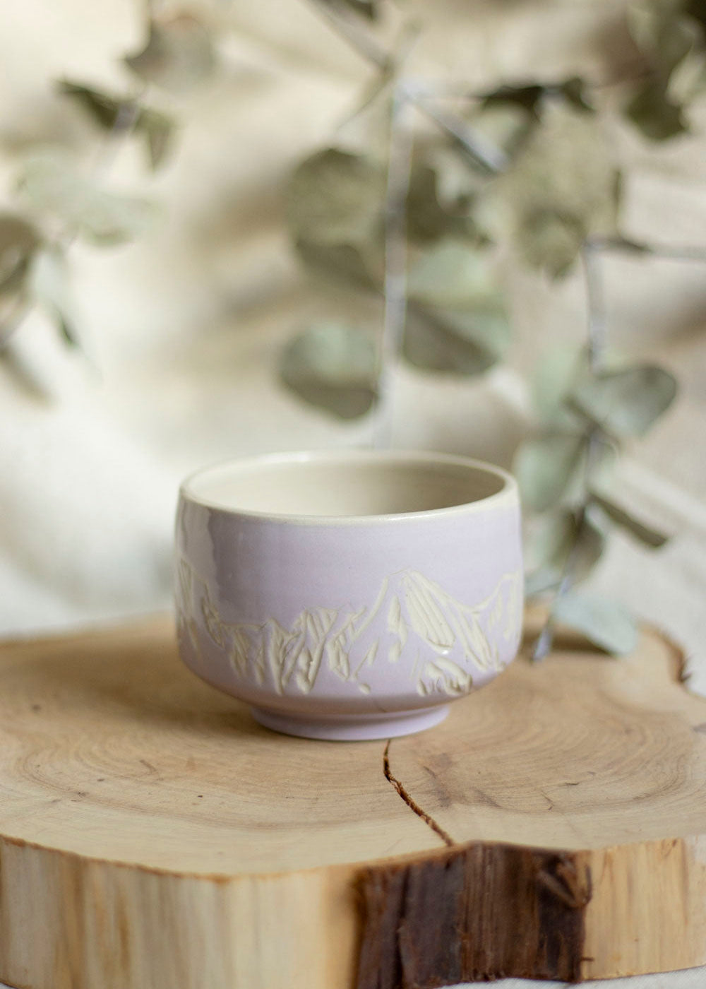 Image d'un bol à thé lilas. Le bol est décoré en utilisant la technique du sgraffito et est gravé de paysages de Montagnes. 